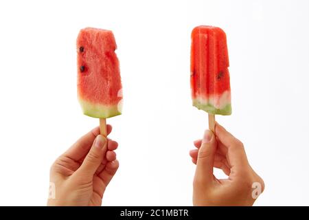 Hände eines Mädchens, das zwei appetitliche, frische Scheiben Wassermelone auf einem Stock auf weißem Hintergrund hält. Das Konzept der gesunden hom Stockfoto