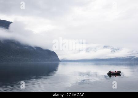Kleines Boot an einem nebligen ruhigen See mit Bergen im Hintergrund Stockfoto