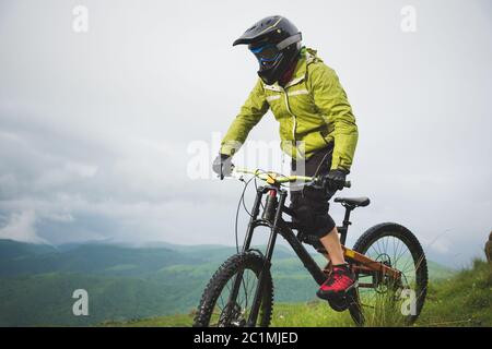 Ein Mann in einem Berghelm mit dem Mountainbike fährt um die schöne Natur bei bewölktem Wetter. Bergab Stockfoto