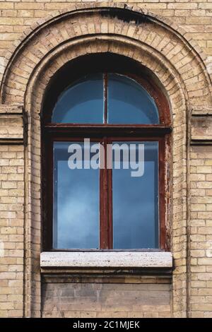 Vintage Bogenfenster in der Wand aus gelben Ziegel. Schwarzes Glas in einem kastanienbraunen dunkelroten Holzrahmen. Das Konzept des antiken Jahrgangs Stockfoto