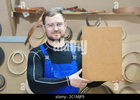 Der Hersteller von Möbeln in Spezialkleidung und Brille hält am Arbeitsplatz eine leere Tafel für den Text. Handwerk p Stockfoto