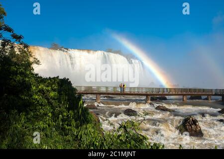 Paar in Fußbrücke mit Regenbogen im Iguazu Falls Nationalpark Stockfoto