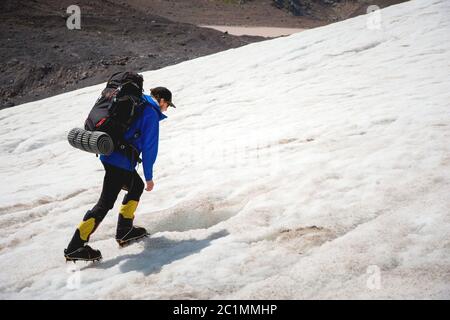 Ein Bergsteiger mit Rucksack geht in Steigeisen entlang eines staubigen Gletschers mit Gehwegen in den Händen zwischen Rissen in der Stockfoto
