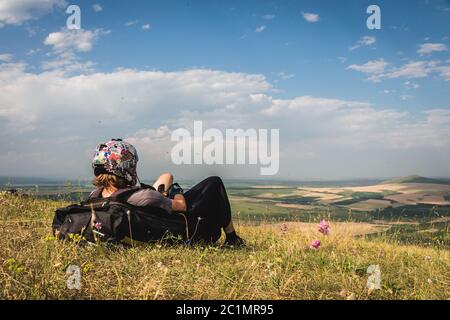 Ein professioneller Gleitschirm in voller Ausrüstung und ein Helm liegt und ruht auf dem Gras hoch in den Bergen und schaut auf die Wolken Stockfoto