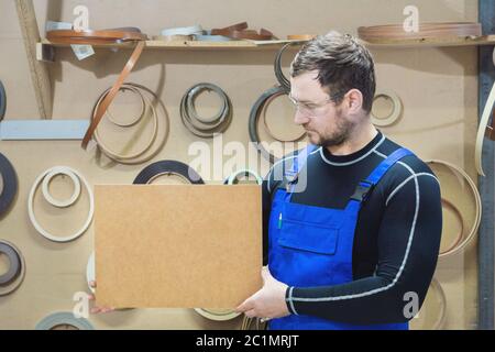 Der Hersteller von Möbeln in Spezialkleidung und Brille hält am Arbeitsplatz eine leere Tafel für den Text. Handwerk p Stockfoto