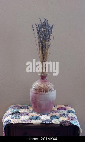 Hohes getrocknetes Lavendel Bouquet von Kräuterblumen in einer Keramikvase auf einem antiken Tischbezug mit grauem Hintergrund. Stockfoto