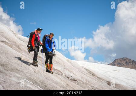 Zwei Touristen, ein Mann und eine Frau mit Rucksäcken und Katzen auf den Füßen, stehen auf dem Eis im Hintergrund der Berge von Th Stockfoto