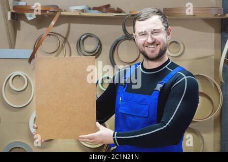 Der Hersteller von Möbeln in Spezialkleidung und Brille hält am Arbeitsplatz eine leere Tafel für den Text. Handwerk p Stockfoto