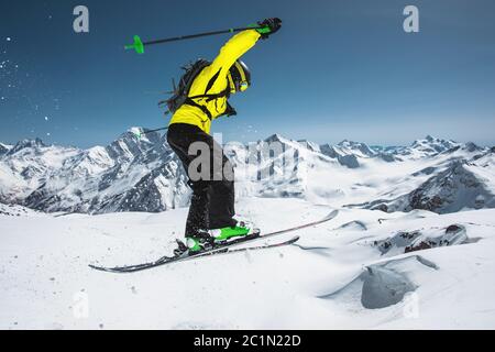 Ein Skifahrer in voller Sportausrüstung springt in den Abgrund von der Spitze des Gletschers vor dem Hintergrund des blauen Himmels und der Stockfoto