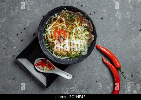 Asiatische Küche, Rindersuppe auf schwarzem Teller auf dunklem Hintergrund. Suppe Fo mit würziger Rinderbrühe, Rinderfilet, udon-Nudeln, Chiliplaste Stockfoto