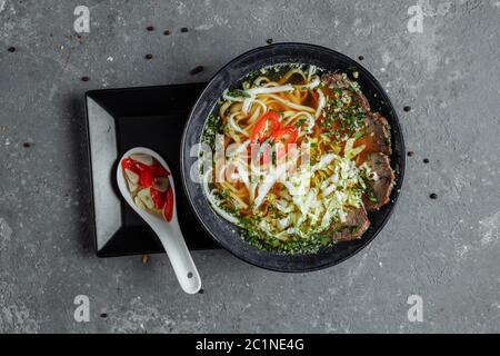 Asiatische Küche, Rindersuppe auf schwarzem Teller auf dunklem Hintergrund. Suppe Fo mit würziger Rinderbrühe, Rinderfilet, udon-Nudeln, Chiliplaste Stockfoto
