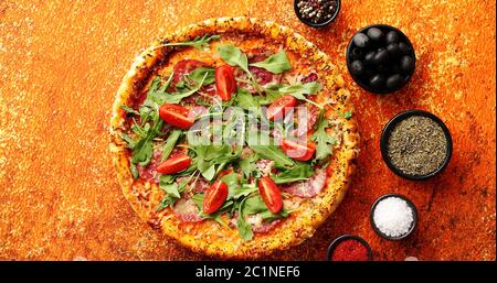 Leckere Pizza auf einem rostigen Hintergrund mit Gewürzen, Kräutern und Gemüse Stockfoto