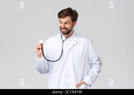 Krankenhaus, medizinisches Personal, covid-19 Behandlungskonzept. Schöner Arzt mit Bart in weißen Peelings, trägt Stethoskop Patienten Lunge zu hören Stockfoto