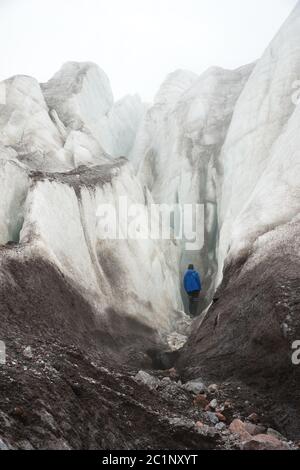 Ein Freikletterer mit einer Eispickel in der Hand steht am Fuße des Großen Gletschers neben einem epischen Riss im Nebel in der Monta Stockfoto