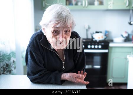 Frustrierte grauhaarige alte Frau in ihrem Haus am Tisch. Stockfoto