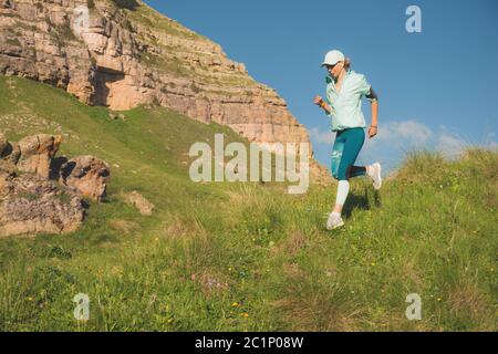 Attraktive Sportmädchen in einer Kappe und Kopfhörer Joggen in einem malerischen Ort den Hügel in der Nähe der Felsen bei Sonnenuntergang. Workout ou Stockfoto