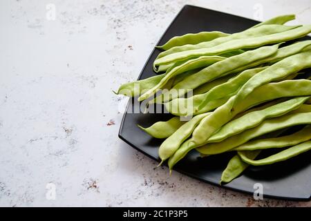 Schwarzer Keramik Teller mit frischen grünen Bohnen Kaffeepads Stockfoto