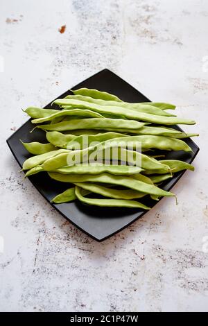 Schwarzer Keramik Teller mit frischen grünen Bohnen Kaffeepads Stockfoto