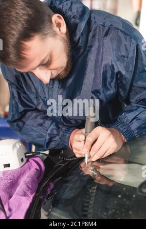 Nahaufnahme Auto Glasur Arbeiter Befestigung und Reparatur einer Windschutzscheibe oder Windschutzscheibe eines Autos an einer Garage Service-Station. Glas bohren Stockfoto