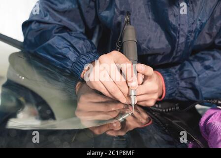 Nahaufnahme Auto Glasur Arbeiter Befestigung und Reparatur einer Windschutzscheibe oder Windschutzscheibe eines Autos an einer Garage Service-Station. Glas bohren Stockfoto