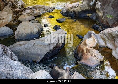 Kleiner Bach mit klarem und gelbem Wasser, das durch die Felsen fließt Stockfoto