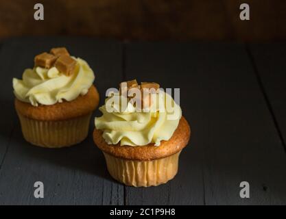 Zwei butterscotch Caramel fudge Cup Cakes auf rustikalen Schwarzer Tisch mit selektiven Fokus eingerichtet Stockfoto