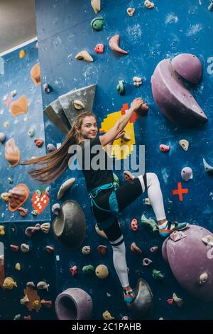 Junge Frau, die eine große, von Männern gemachte Kletterwand klettert Stockfoto