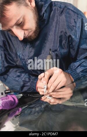 Nahaufnahme Auto Glasur Arbeiter Befestigung und Reparatur einer Windschutzscheibe oder Windschutzscheibe eines Autos an einer Garage Service-Station. Glas bohren Stockfoto