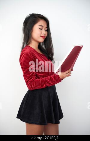 Schöne asiatische Frau mit langen Haaren trägt schwarzen Minirock Lesebuch, weißen Hintergrund Studio erschossen Stockfoto