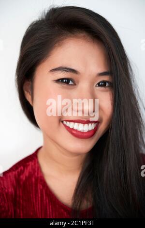 Vertikale Nahaufnahme Studio Porträt von fröhlich attraktive junge asiatische Frau mit dunkelroten Lippen Blick auf Kamera lächelnd, weißen Hintergrund Stockfoto