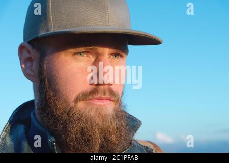 Nahaufnahme eines bärtigen, stilvollen Reisenden in einer Mütze vor blauem Himmel. Konzept der Zeit bis zur Reise Stockfoto