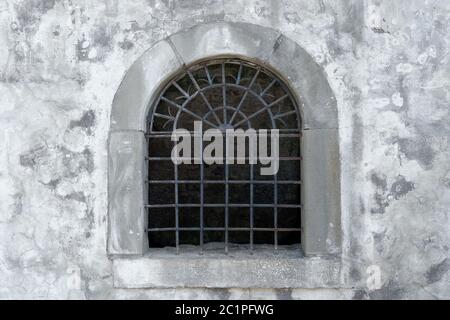 Altes halbkreisförmiges offenes Gitterfenster in der grauen Fassade eines mittelalterlichen Gebäudes Stockfoto