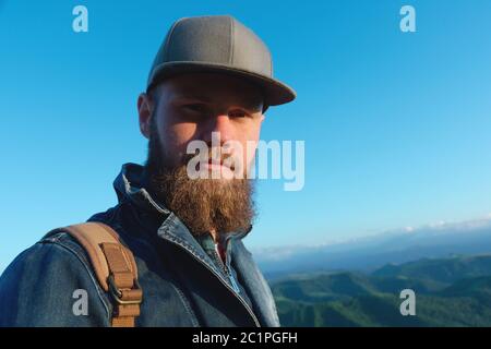 Porträt eines bärtigen stilvollen Reisenden in einer Mütze gegen einen blauen Himmel. Konzept der Zeit bis zur Reise Stockfoto