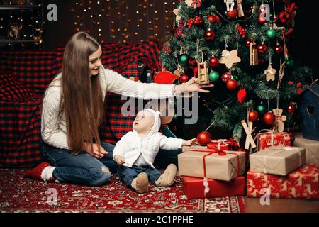 Liebevolle Mutter schmücken Weihnachtsbaum mit Baby. Stockfoto