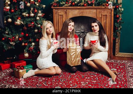 Drei Frauen sitzen neben Kamin und weihnachtsbaum Stockfoto