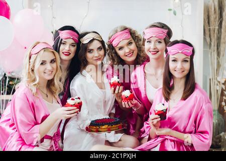 Hübsche Mädchen in rosa Roben und schlaf Masken mit Desserts im brautduschen. Stockfoto