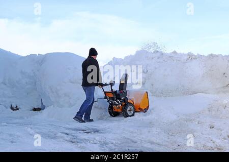 Ein Mann mit einem Schneegebläse räumt hohen Schnee Stockfoto