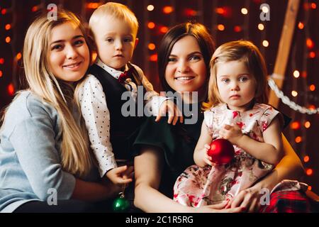 Zwei Mütter sitzen mit niedlichen Kinder Weihnachtsgeschenke. Stockfoto