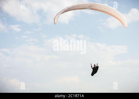 Der professionelle Gleitschirm im Kokon-Anzug fliegt hoch über dem Boden gegen den Himmel Stockfoto