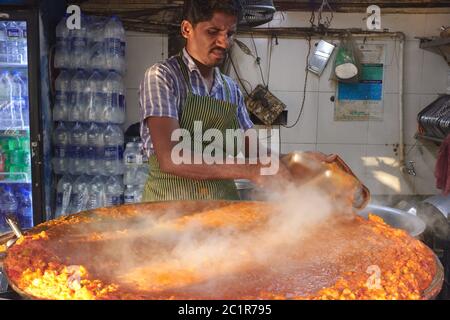 Ein Koch an einem Imbissstand in Mumbai, Indien, auf einer großen Kochplatte (tawa), die Bhaji (würzige Gemüsestaische) zur Herstellung von beliebten lokalen Snack-Artikel Pav Bhaji macht Stockfoto