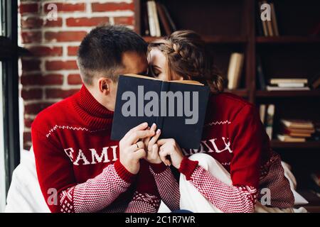 Paar im Winter Jumper küssen, der sich hinter dem Buch. Stockfoto