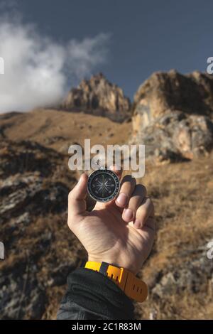 Ein männlicher Wanderer sucht im Herbst eine Richtung mit einem magnetischen Kompass in den Bergen. Blickpunkt. Mann's Hand Witz Stockfoto