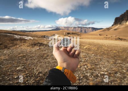 Ein männlicher Wanderer sucht im Herbst eine Richtung mit einem magnetischen Kompass in den Bergen. Blickpunkt. Mann's Hand Witz Stockfoto