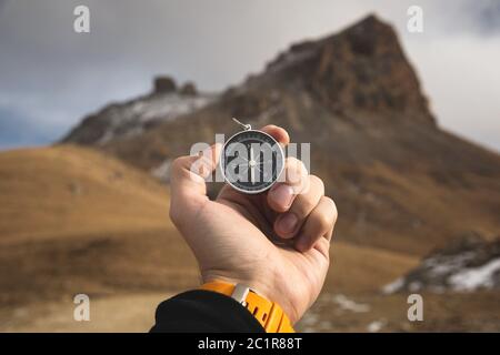 Ein männlicher Wanderer sucht im Herbst eine Richtung mit einem magnetischen Kompass in den Bergen. Blickpunkt. Mann's Hand Witz Stockfoto