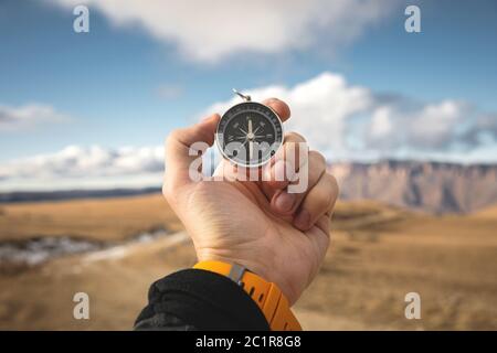 Ein männlicher Wanderer sucht im Herbst eine Richtung mit einem magnetischen Kompass in den Bergen. Blickpunkt. Mann's Hand Witz Stockfoto