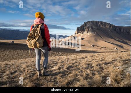 Portrait von der Rückseite eines Mädchen Reisenden in einer Jacke mit einer Kappe und einem Rucksack steht auf dem Hintergrund einer epischen Landschaft wi Stockfoto