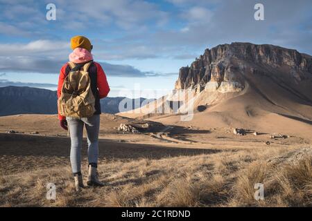 Portrait von der Rückseite eines Mädchen Reisenden in einer Jacke mit einer Kappe und einem Rucksack steht auf dem Hintergrund einer epischen Landschaft wi Stockfoto