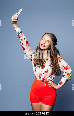 Attraktive Frau in floralen Hemd und roten Shorts, die Selbstporträt über violetten Hintergrund. Stockfoto