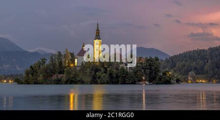 Bleder See mit Marienkirche und Bergen im Hintergrund unter stürmischem Himmel mit Blitz in der Dämmerung, Slowenien, Europa Stockfoto