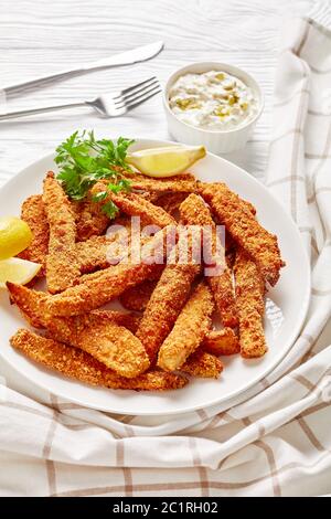 Panierte und frittierte servierte Fischstäbchen, Fischfiletfinger auf einem weißen Teller auf einem Holztisch mit Tartarsauce und Zitronenkeilen, vertikale Ansicht Stockfoto